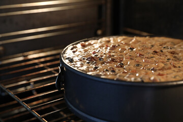 A close up large round traditional Christmas cake in the oven slowly baking or cooking. A variety of fruit visible on the still wet moist surface.