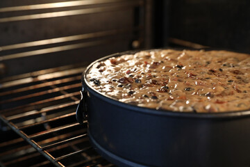A close up large round traditional Christmas cake in the oven slowly baking or cooking. A variety...