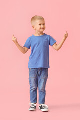 Adorable little boy in blue t-shirt pointing at something on pink background