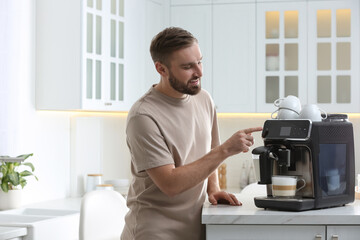 Young man preparing fresh aromatic coffee with modern machine in kitchen