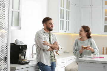 Young man talking with his girlfriend while using modern coffee machine in kitchen