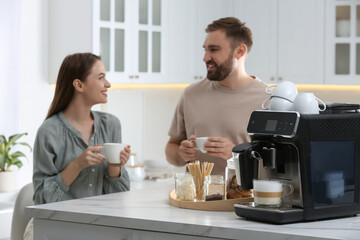 Fototapeta na wymiar Happy couple enjoying fresh aromatic coffee in kitchen, focus on modern machine