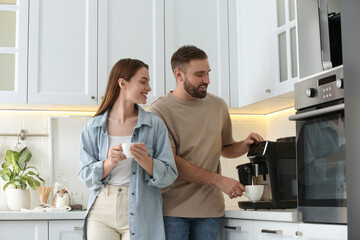 Happy couple preparing fresh aromatic coffee with modern machine in kitchen