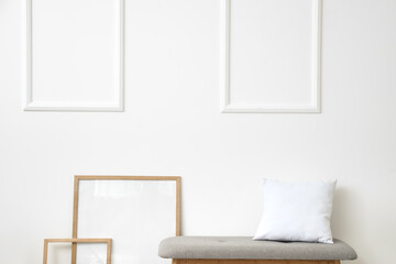 Comfortable bench with pillow and frames near light wall