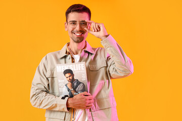 Young man in stylish jacket with magazine on yellow background