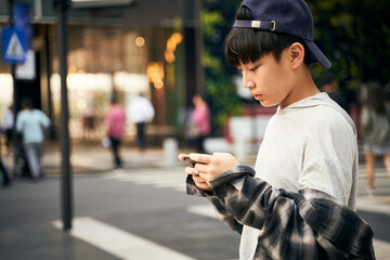 teenage asian boy using mobile phone outdoors on street
