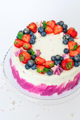 Delicate cake decorated with fresh berries strawberries blueberries white plain background. Festive dessert with berries