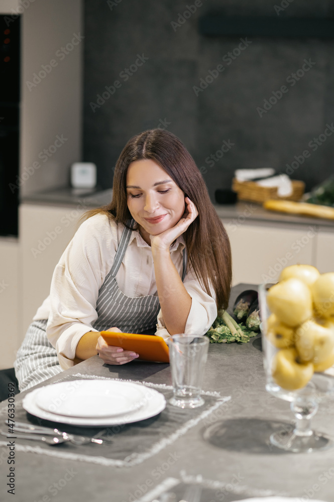 Wall mural young woman sitting in the kitchen and watching something on internet