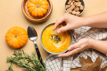 Woman eating tasty pumpkin cream soup on beige background