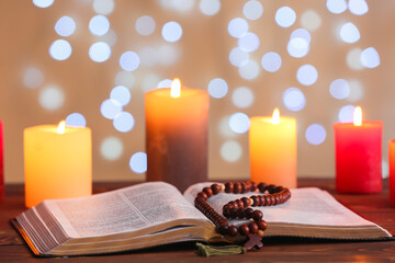 Book with beads and glowing candles on table against blurred lights. Christmas story