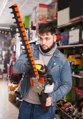 young serious man with an electric brush cutter in hardware store