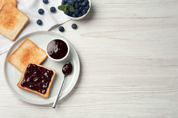 Toasts and blueberry jam served on white wooden table, flat lay. Space for text