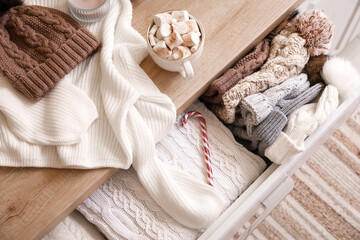 Chest of drawers with winter clothes and cup of hot chocolate in room