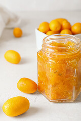 Jar of tasty kumquat jam and fresh fruits on light background
