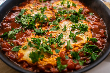 Shakshouka with tomatoes, peppers eggs, on a hot pan with crout croutons sprinkled with chives