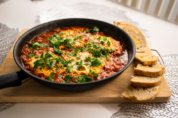 Shakshouka with tomatoes, peppers eggs, on a hot pan with crout croutons sprinkled with chives