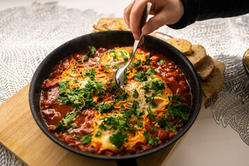 Shakshouka with tomatoes, peppers eggs, on a hot pan with crout croutons sprinkled with chives