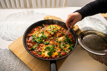 Shakshouka with tomatoes, peppers eggs, on a hot pan with crout croutons sprinkled with chives