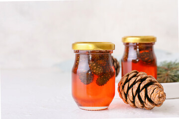 Jars of tasty pine cone jam on light background