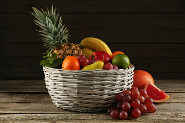Fresh ripe fruits and wicker bowl on wooden table