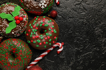 Tasty Christmas donuts with balls and candy cane on dark background