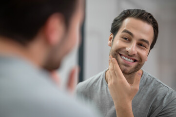 A young man in grey tshirt looking at his reflection in the mirror