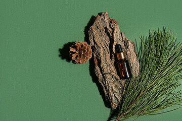 Composition with bottle of essential oil, tree bark, pine cone and branch on green background