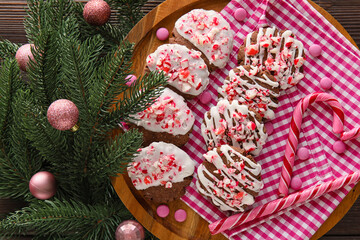 Board with tasty candy cane cookies, fir branch and Christmas balls on dark wooden background, closeup