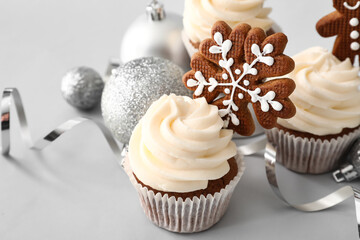 Tasty Christmas cupcakes with gingerbread cookies on light background