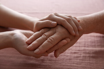 Young and elderly women holding hands together on pink fabric, closeup