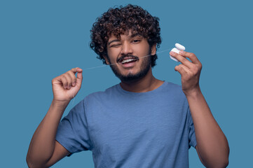 Bearded curly-haired mustached man flossing his teeth