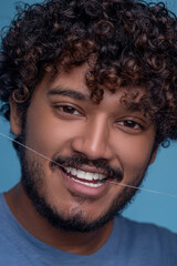 Pleased cute young man using dental floss