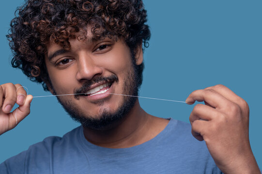 Smiling guy with curly hair flossing his teeth Stock Photo | Adobe Stock