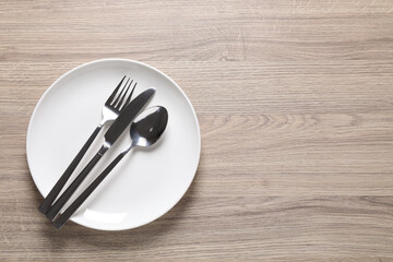 Plate with shiny silver cutlery on wooden table, top view. Space for text