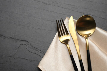 Set of golden cutlery with napkin on black table, top view. Space for text - obrazy, fototapety, plakaty