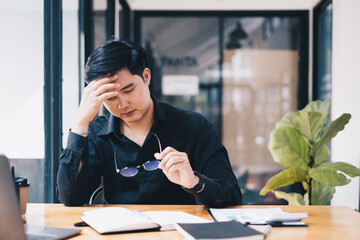Portrait of stressed out businessman sitting at desk and take off glasses Global economic problems concept.
