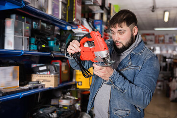 Glad positive smiling confident buyer chooses an electric tool in hardware store