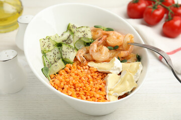 Delicious lentil bowl with shrimps, soft cheese and cucumber on white wooden table