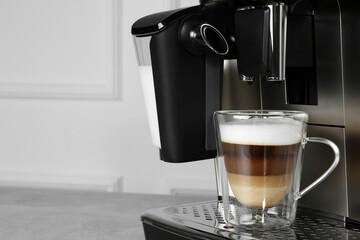 Modern coffee machine with glass cup of latte on grey table near white wall, closeup. Space for text