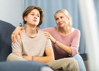 Obraz premium Upset teenager boy after quarrel with his mother in domestic interior, mother consoles son