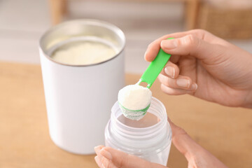 Obraz na płótnie Canvas Woman preparing infant formula at table indoors, closeup. Baby milk