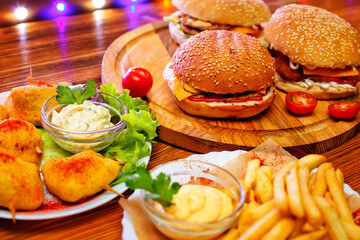 American food. hamburger with bacon and cheese with beef patty tomatoes and onions. burgers and French fries with sauce on a wooden table against the background of lights.