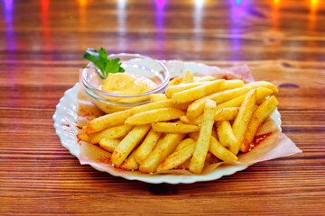 French fries in a bowl on a wooden background with sauce. With multicolored lights on the background.