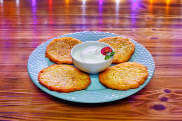 Potato pancakes or latkes on a blue plate of rustic wooden surface with sour cream
