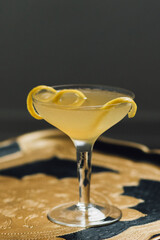 yellow cocktail in coupe glass with lemon twist on gold tray