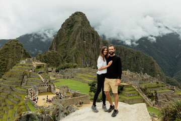 Happy couple poses in front of ruins of inca's citadel Machu Picchu in Peru - obrazy, fototapety, plakaty