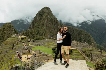 Papier Peint photo Machu Picchu Happy couple poses in front of ruins of inca's citadel Machu Picchu in Peru