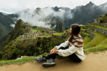 A young woman sitting on the natural terrace and looking at the Machu Picchu ruins
