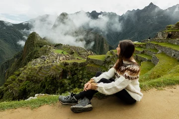 Cercles muraux Machu Picchu A young woman sitting on the natural terrace and looking at the Machu Picchu ruins