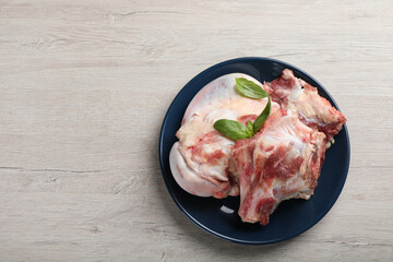 Plate with raw chopped meaty bones and basil on white wooden table, top view. Space for text